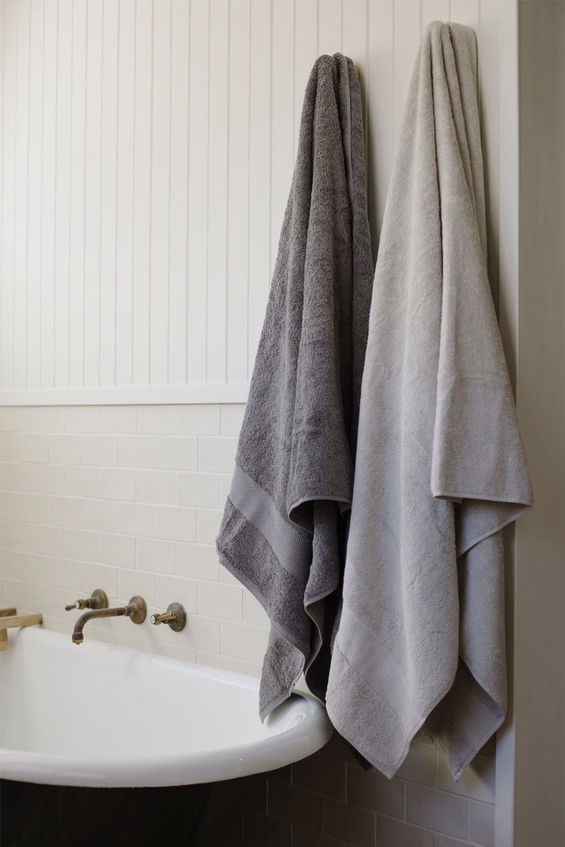 Two gray towels hanging on a towel rack above a white sink with gold fixtures.